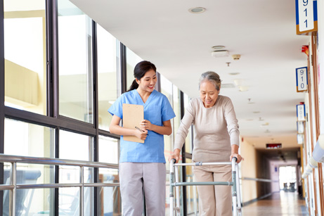 A caregiver and a patient walking down the hall of a nursing homes or long-term care facility